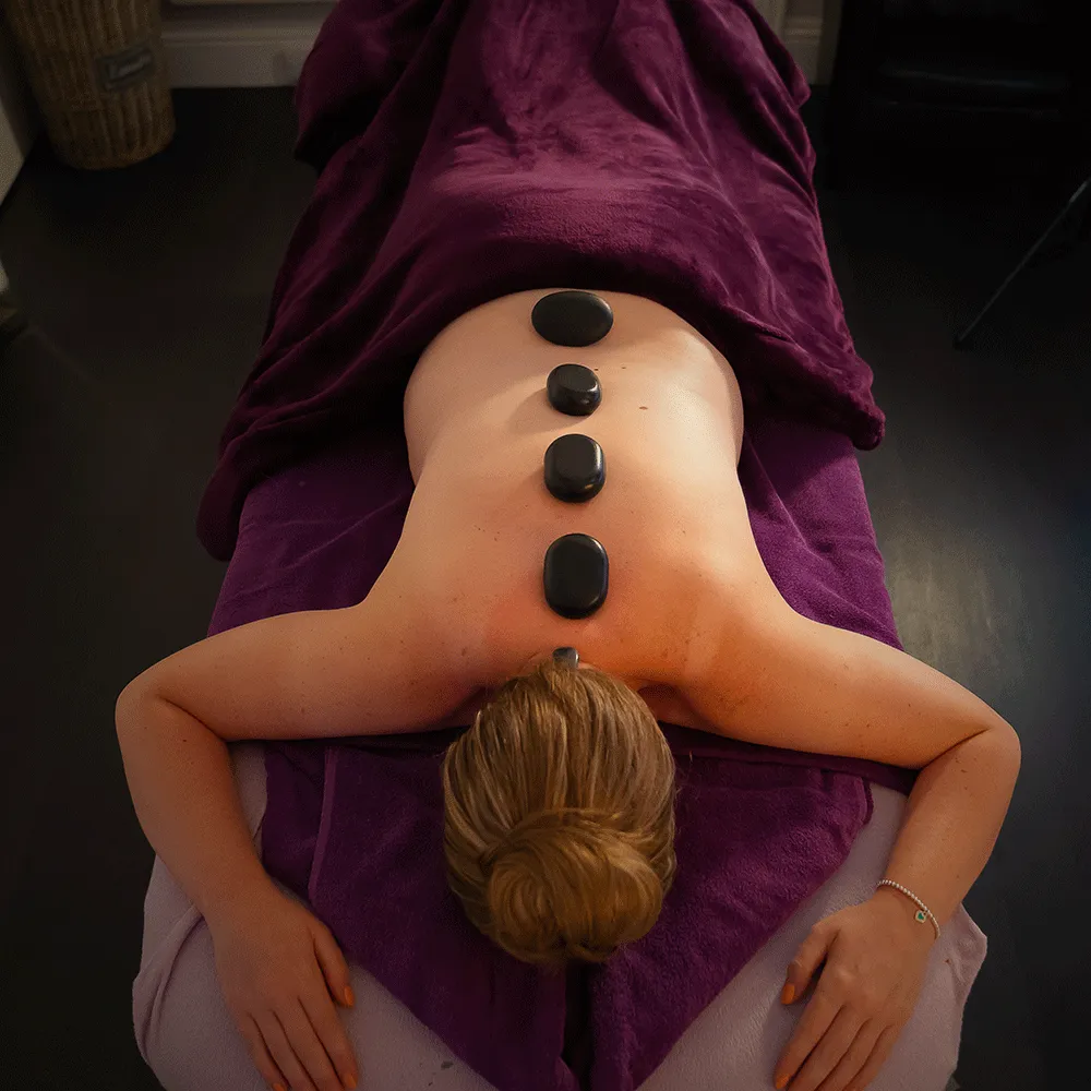 A lady laying on the massage bed with 4 hot stones along her spine